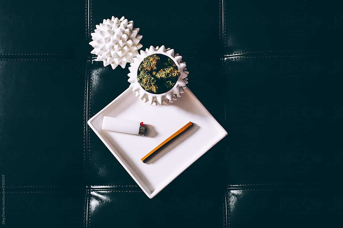 Aesthetic white ceramic rolling tray with a lighter, joint and jar of cannabis on it.