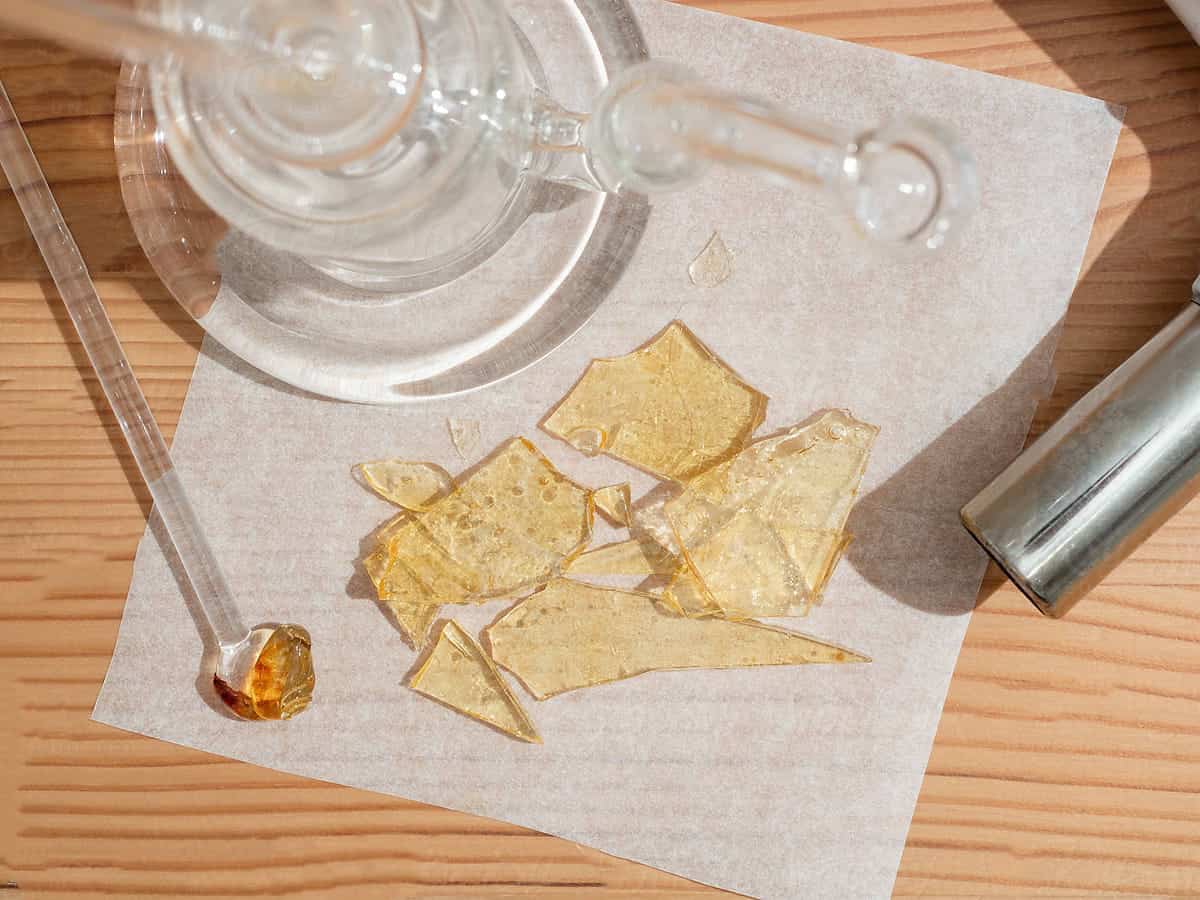 some glass or shatter cannabis concentrate is pictured next to a dab rig and a dab tool that's been used