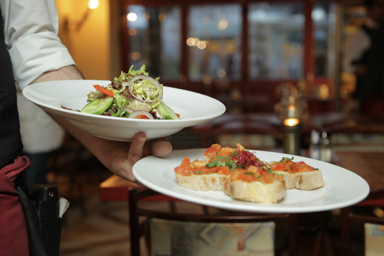 Upclose of waiter holding two white plates with fancy food.