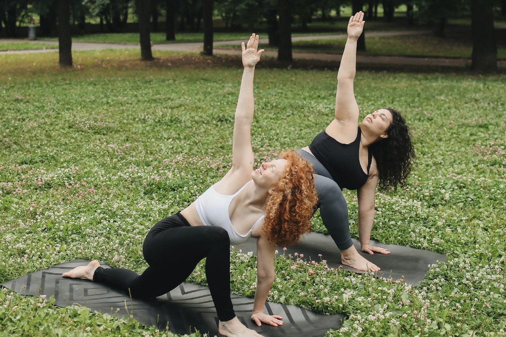 Two women practicing yoga on the grass at a park.