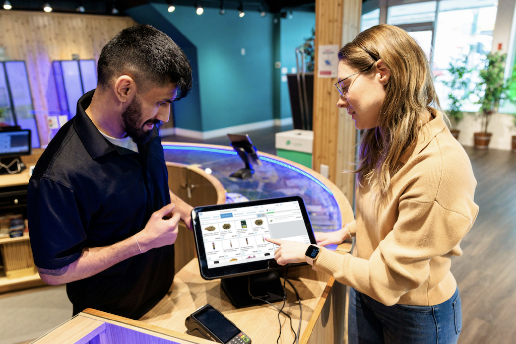 Male budtender helping a female customer buy cannabis on a digital menu.