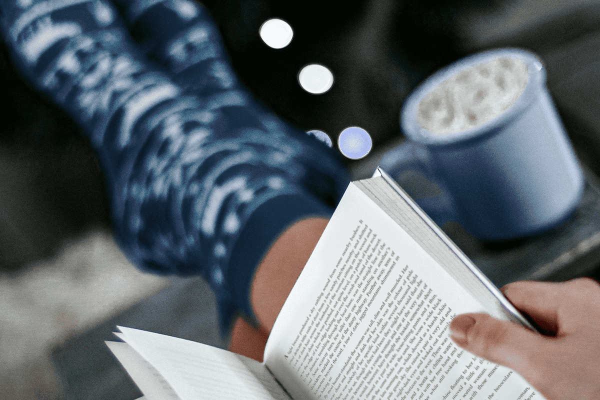 Woman reading a cozy book and sipping a hot chocolate.