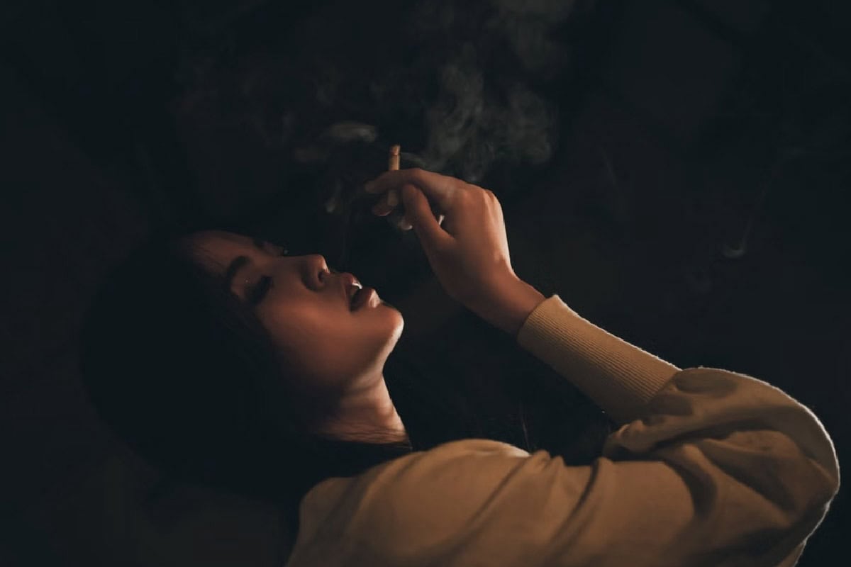 Asian woman smoking a joint while laying down in the dark.